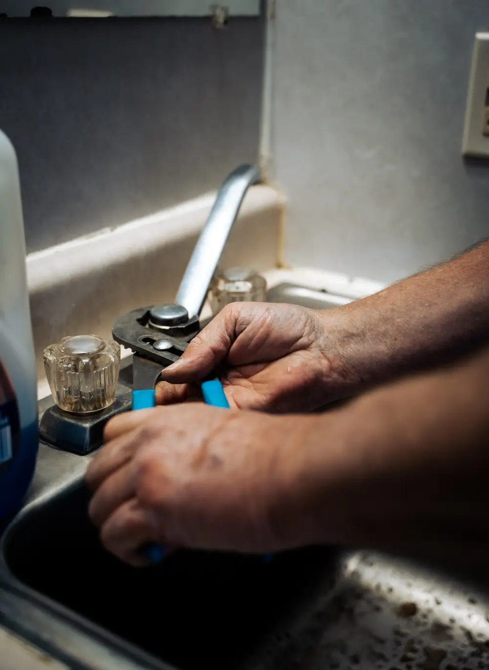 Plumber fixing kitchen faucet with wrench in dimly lit room
