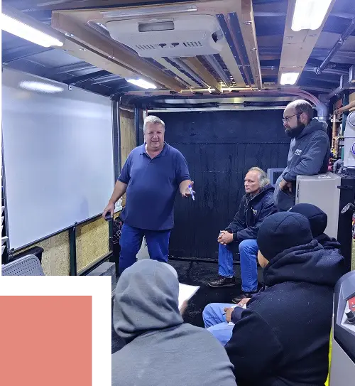 A trainer presenting to a small group of technicians during an HVAC training session inside a mobile classroom trailer.
