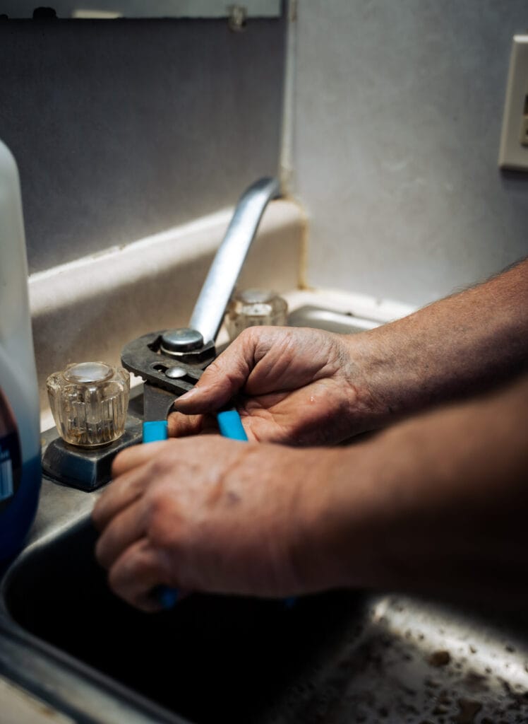 Plumber repairing a bathroom sink faucet with hand tools during residential plumbing maintenance and fixture service